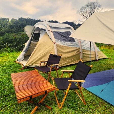 A tent pitched in a beautiful forest with a campfire and camping gear.