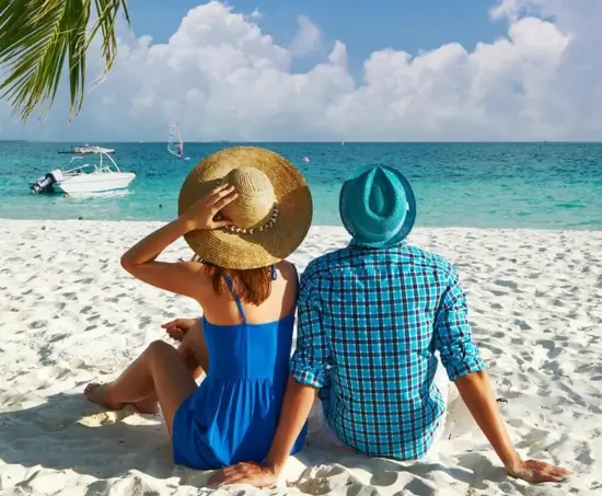 A couple sitting on the pristine white sands of a Malaysian beach, gazing out at the turquoise waters with a sailboat in the distance, embodying the peaceful beach retreats offered by MJ Adventure Travel Services.