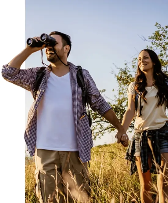 A couple enjoying a nature walk, with the man using binoculars to spot wildlife while holding hands with his partner, showcasing the shared adventures in Malaysia's natural parks with MJ Adventure Travel Services.